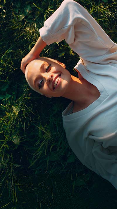 Eine Frau mit kurzen, blonden Haaren liegt im Gras und schaut nach oben den Leser an.