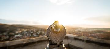 Ein Fernrohr auf einer Stadtmauer zeigt in die Richtung der Häuser.